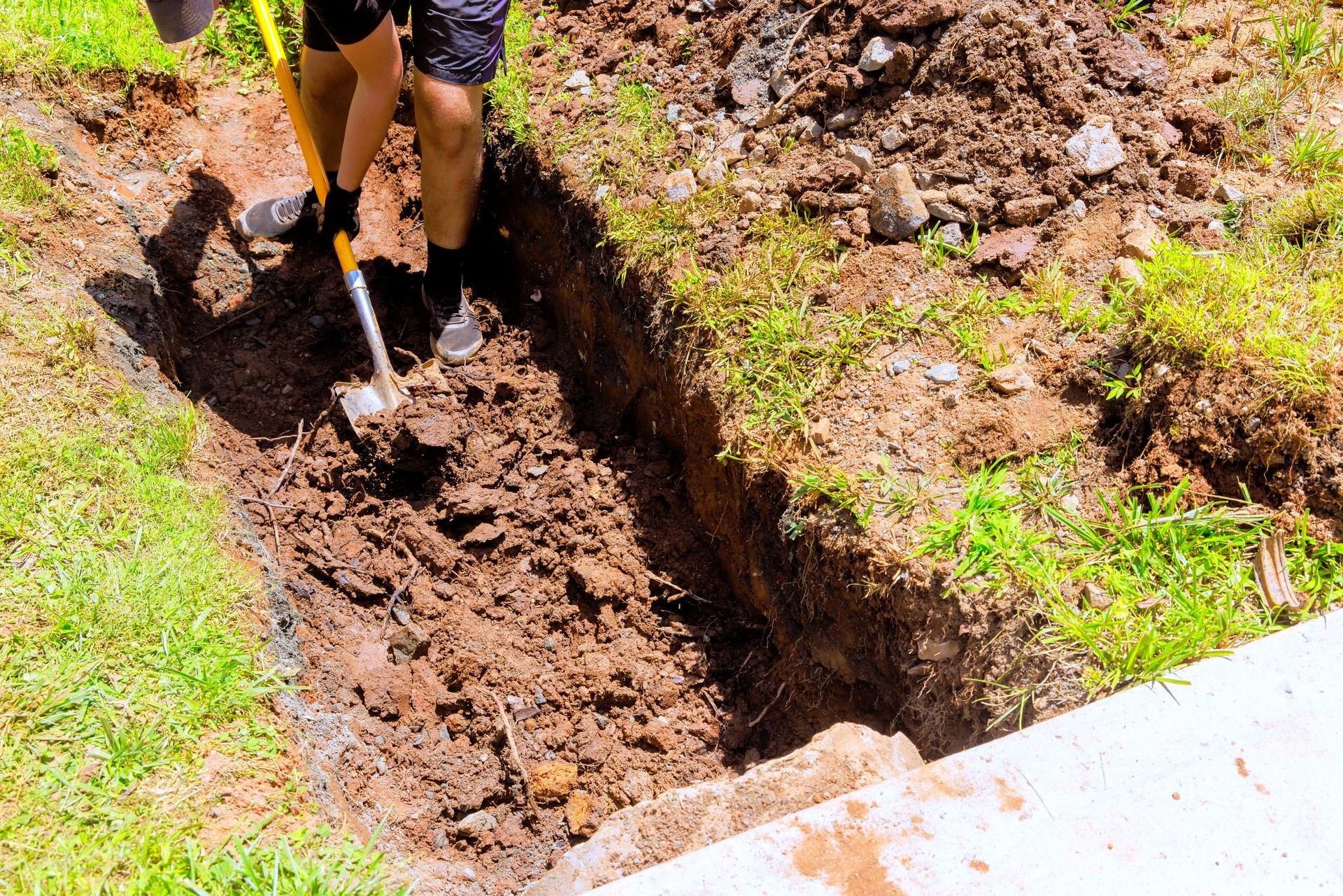 Worker digging trench with shovel for a drainage pipe